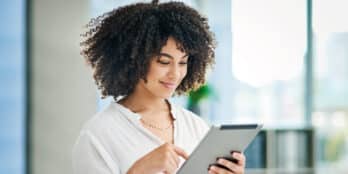 Female senior living community staff member standing and smiling as she looks down at content on a tablet device