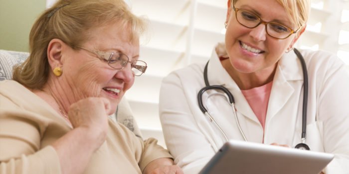 A doctor sitting with a resident reviewing their recovery progress using PointClickCare EHR on a tablet device