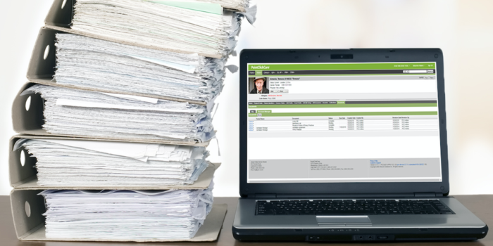 A stack of patient files beside a laptop with PointClickCare's Document Manager Solution on it.