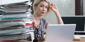 A skilled nursing director of admissions sitting at her desk with a stack of patient documents and her laptop with PointClickCare's document manager