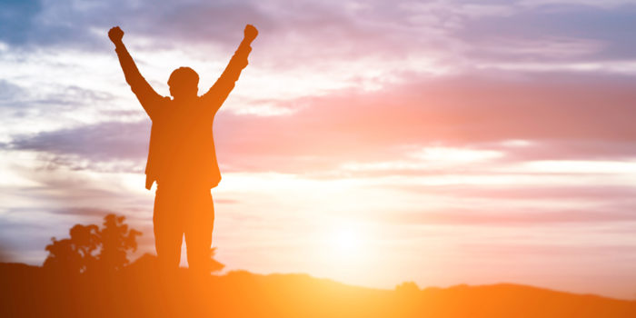 A man standing outside watching the sun rise with his hands in the air