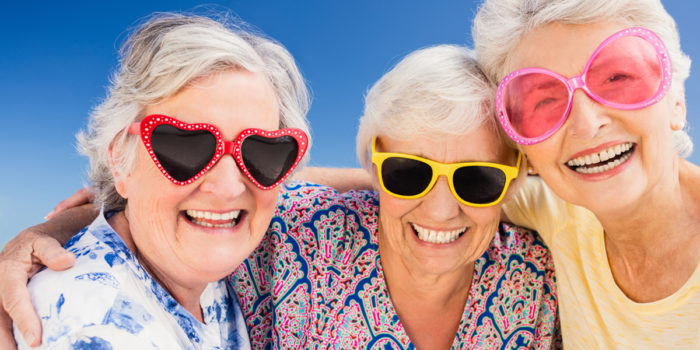 3 elderly women hugging and laughing while wearing funny sun glasses