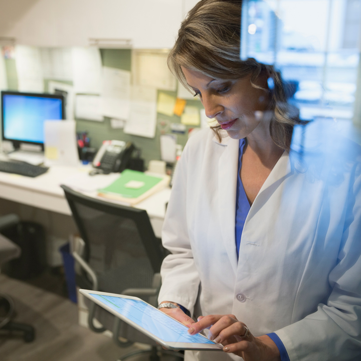 Female doctor standing in her office using PointClickCare's Integrated Direct Messaging app on a tablet device