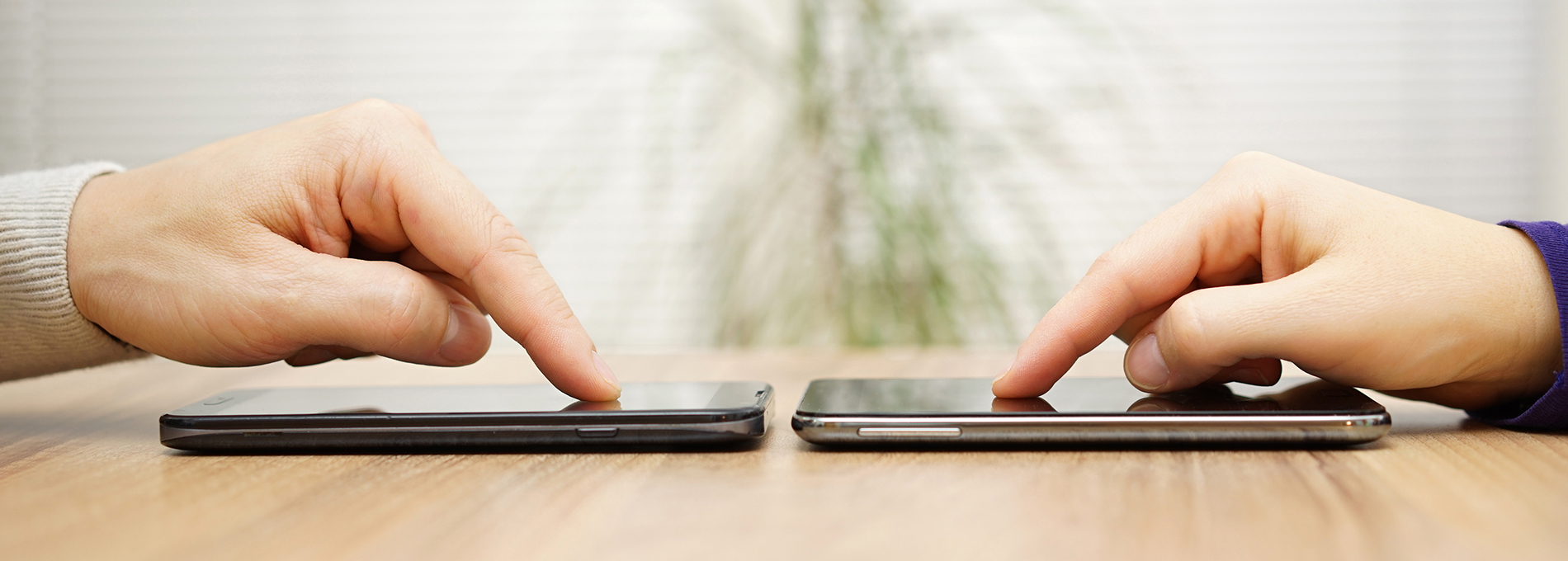 Two smartphone devices placed on a table next to each other with two people placing one of their index fingers on the screen