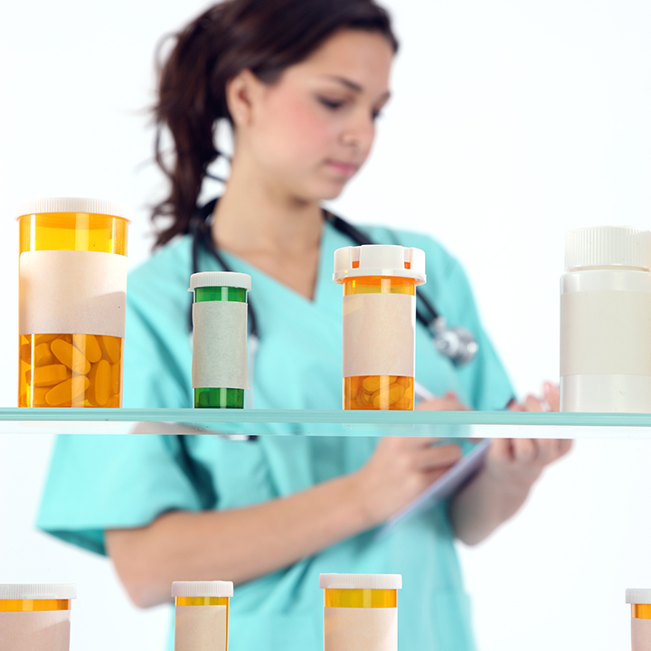 Female skilled nursing provider with a stethoscope around her neck reviewing a patient's prescription with prescription drug bottles in front on shelves