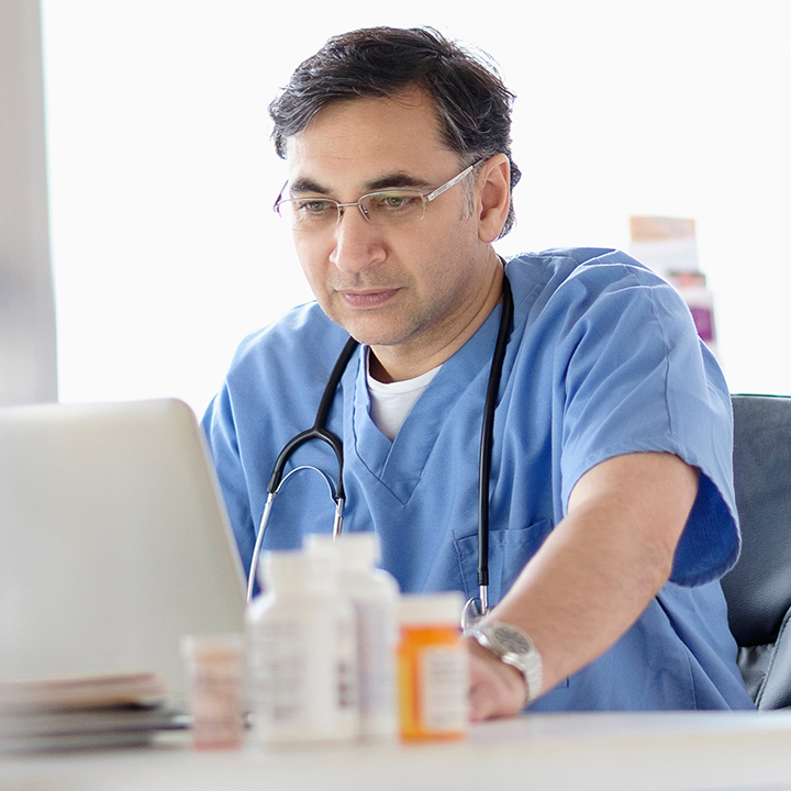 Male doctor sitting looking at patient data in PointClickCare's eMAR software with prescription medication behind it