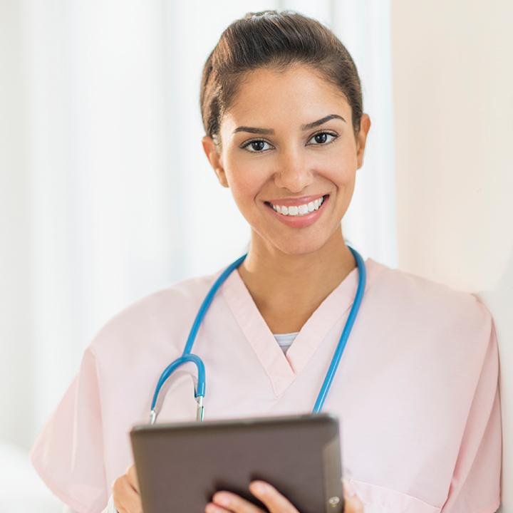 Female skilled nursing provider leaning against a wall smiling while using PointClickCare's eInteract software on a tablet device