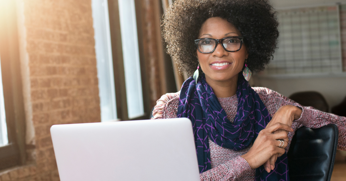 Smiling Black businesswoman posing with laptop at desk