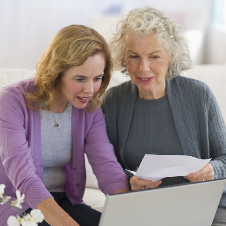 Female home health care provider seated working on a laptop with her home health patient sitting next to her reviewing the content on the laptop