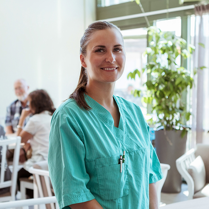 A nurse smiling confidently with some residents sitting around a table in the background