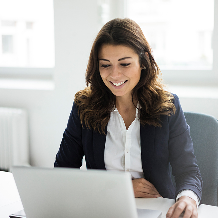A female sales and marketing employee smiling and using the EMR platform on her laptop