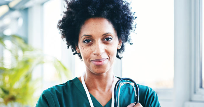 A nurse smiling while holding her stethoscope in her hand