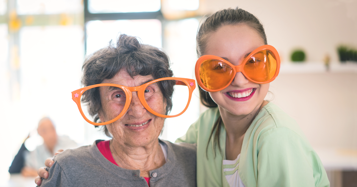A younger woman and older woman smile while wearing large orange glasses