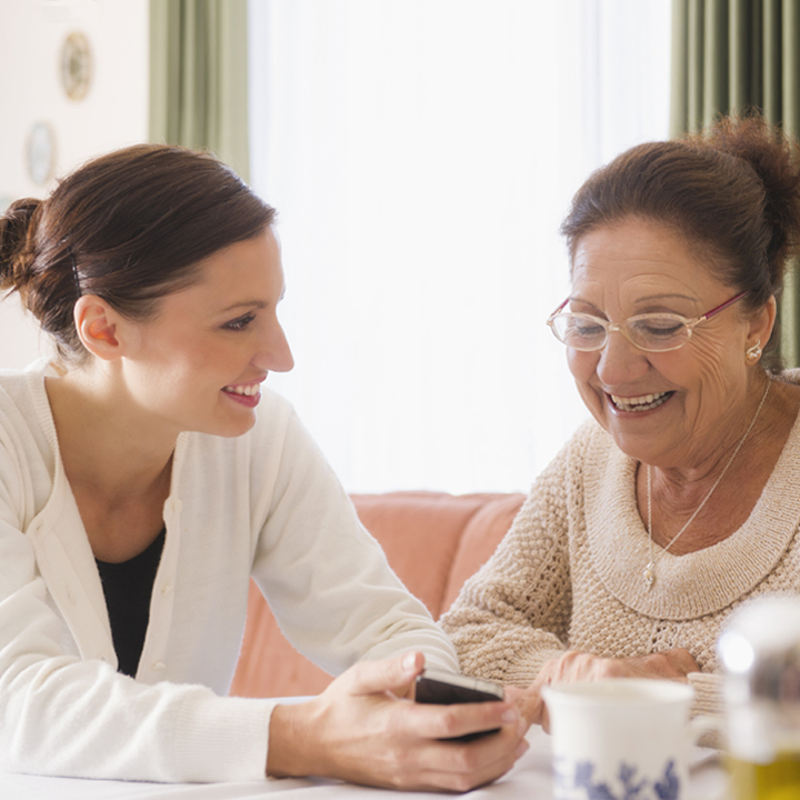 Female senior living care provider seated with a resident laughing as they both view content on a smartphone