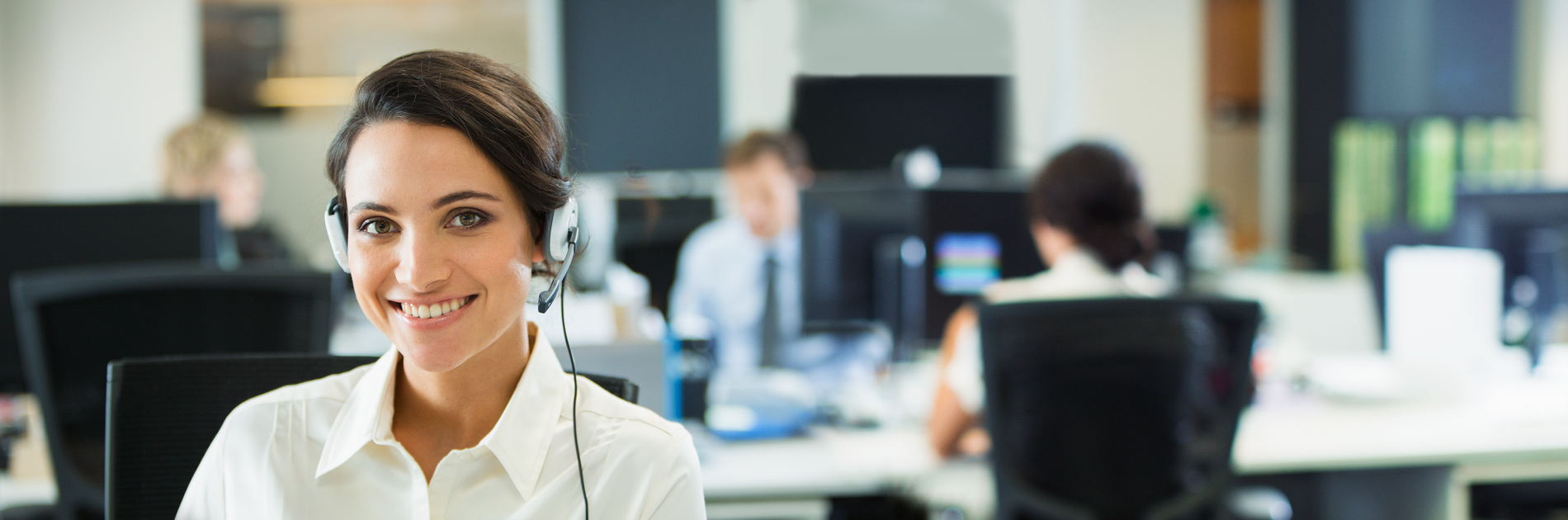 Female customer support representative smiling with a headset on with a blurred background office environment