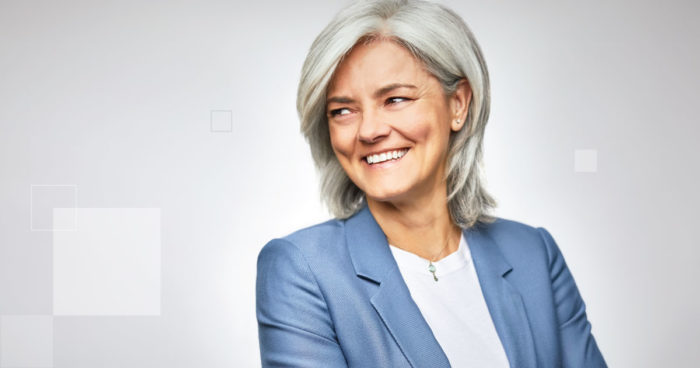 A woman in a blazer smiles and looks off camera.
