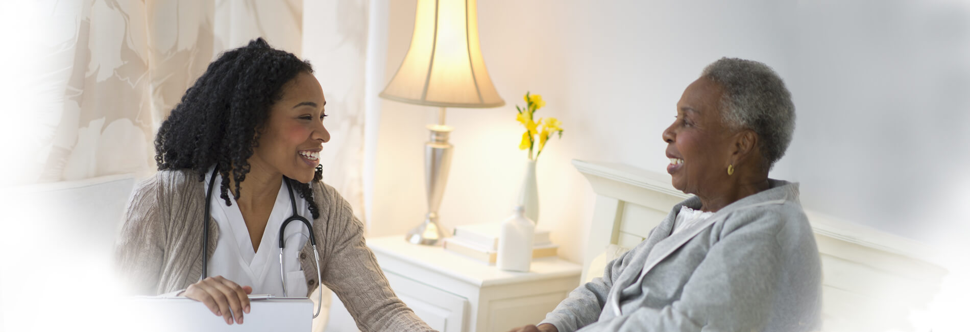A Home Health registered nurse speaking with an elderly client in her bedroom.