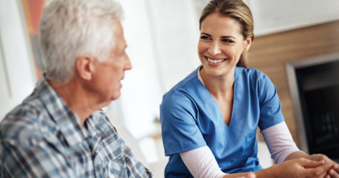 A nurse in a long-term care facility smiles and has a conversation with a male resident.