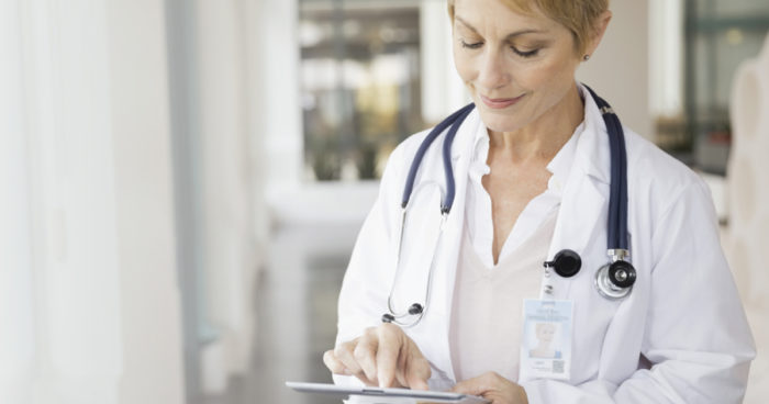 A doctor wearing a white lab coat uses PointClickCare software on her tablet.