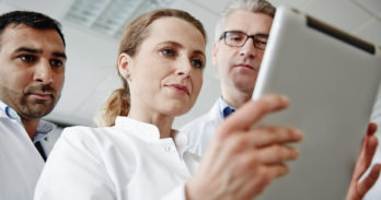 Three doctors in a Skilled Nursing Facility look intently at PointClickCare software on a tablet.