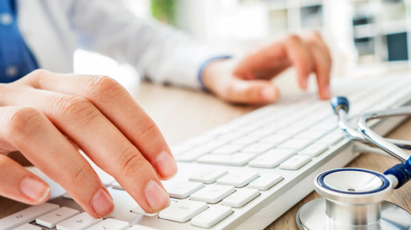 A close-up image of a doctor's hands typing on a computer keyboard.