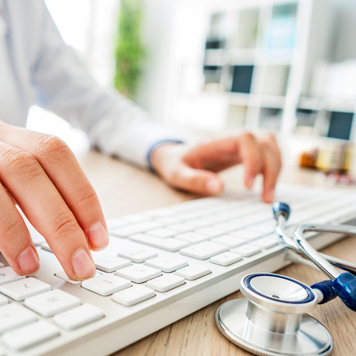 A close up of a doctors hands on a keyboard as they review patient infection information using PointClickCare's Infection Prevention and Control solution on a desktop computer