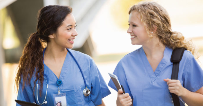 Two female nursing students smile while having a conversation.