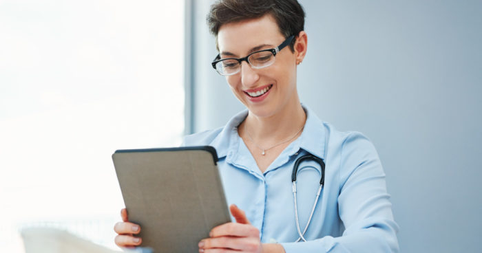 A doctor smiles while using PointClickCare software on a tablet.