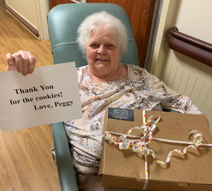 A resident from Seliver Bluff Village seated holding a box of cookies with a thank you sign in one hand