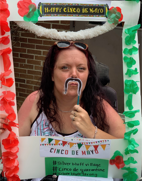 A worker at the Silver Bluff Village posing with a fake moustache and a sign made for Cinco de Mayo