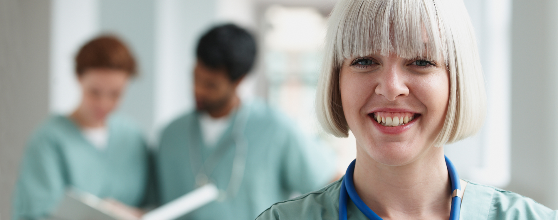 Close up of a nurse smiling with two of her colleagues in the background looking at a medical chart