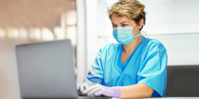 A healthcare worker wearing PPE and using a laptop