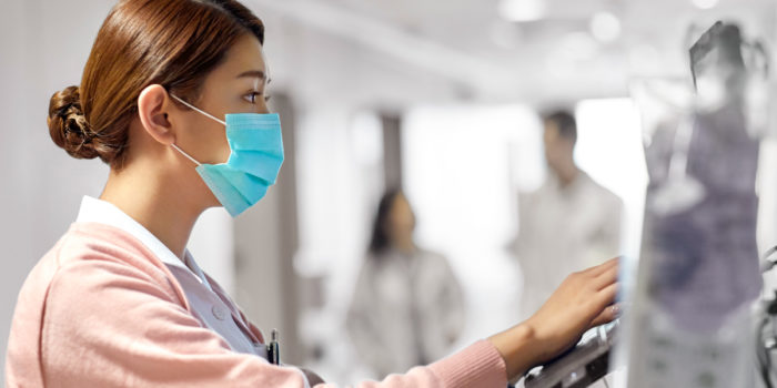 Female nurse wearing a mask reviewing QAPI guidelines on a medical computer