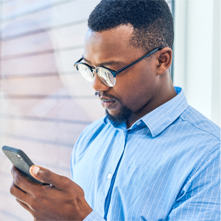 Male standing by a window and looking down at a message on his phone sent through PointClickCare's Automated Care Messaging software