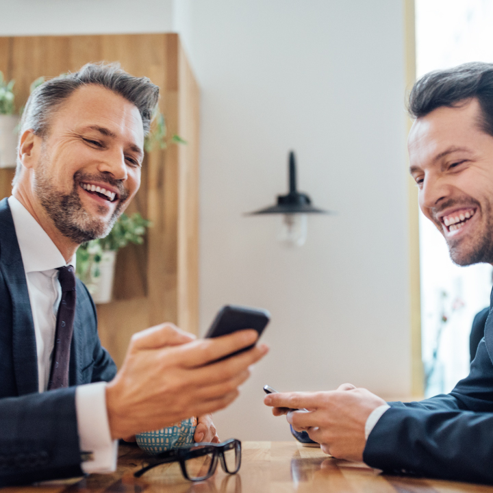 Two businessmen looking at mobile phone and smiling
