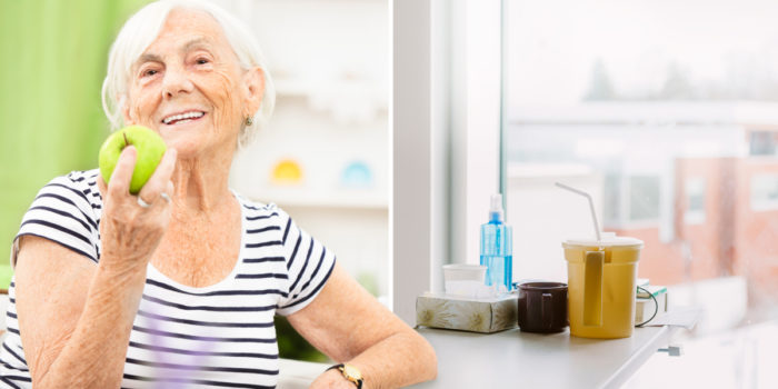 Elderly female leaning against a counter smiling as she eats an apple