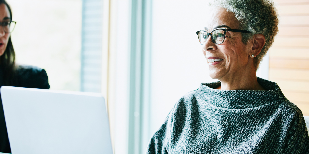 Woman with a laptop open in front of her smiling at someone in the room