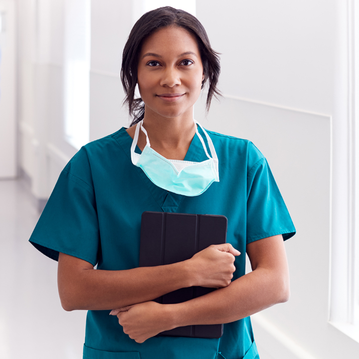 Female clinical nurse standing and holding a tablet device in a hospital corridor