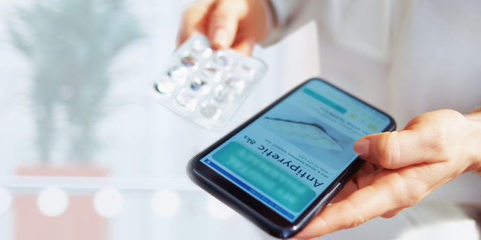 Close up of someone's hands holding a mobile device in one hand and prescription medication in the other hand