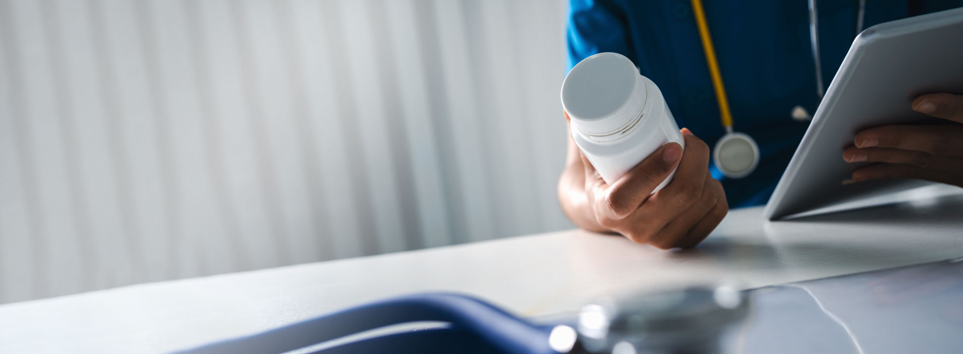 LTPAC nurse holding a medicine bottle and digital tablet with blurred stethoscope on table