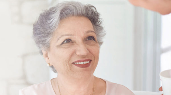 Close up of a senior living resident's face as she looks up and smiles at a care provider in front of her