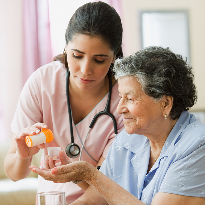Female skilled nursing provider standing next to a female resident and helping her prepare to take her prescription medication