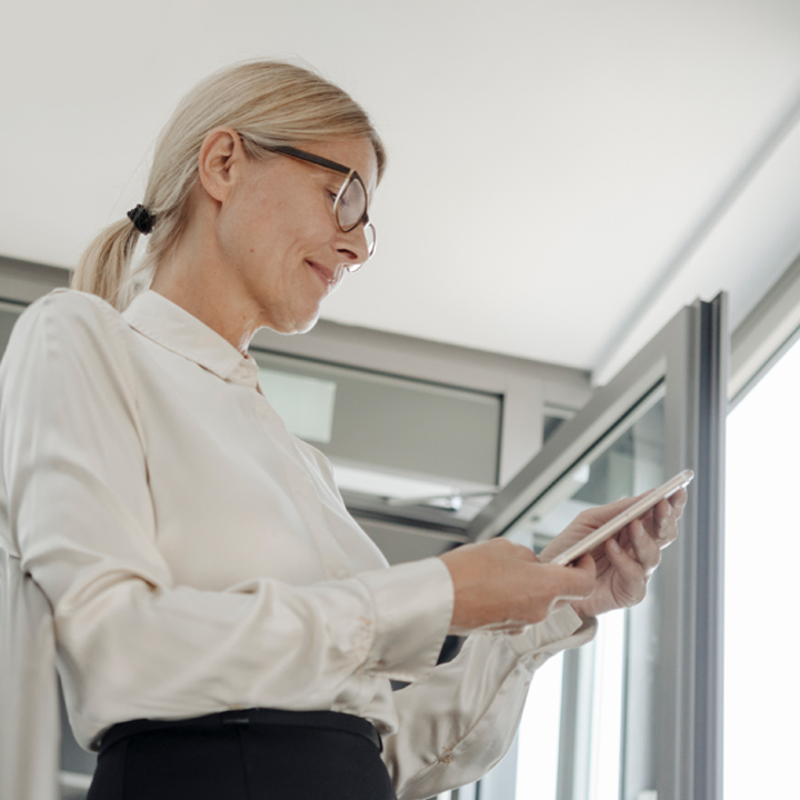 Female executive standing close to a doorway and looking down at her mobile device