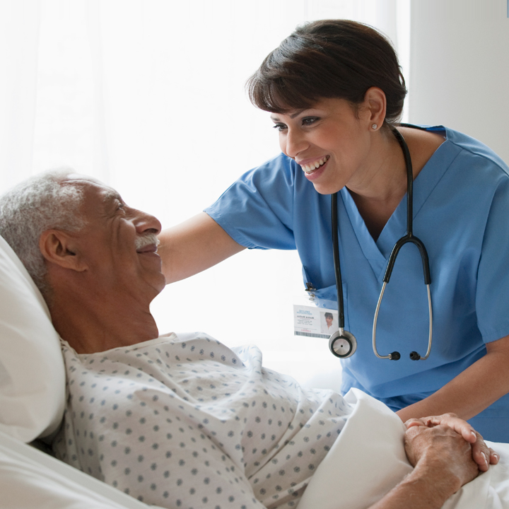 Female skilled nursing provider with stethoscope around her neck smiling as she leans over and cares for a male patient