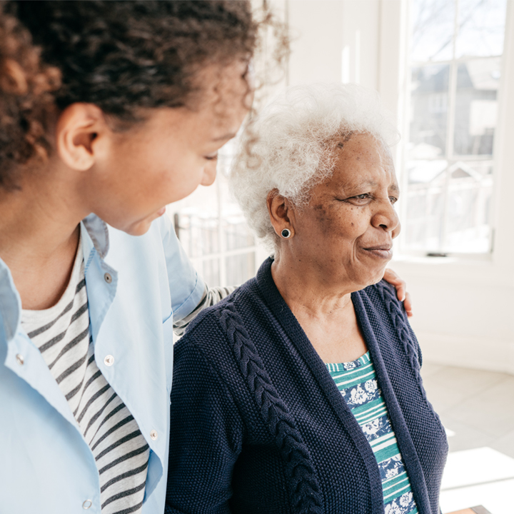 Female senior living care provider standing and smiling with a female resident while having her arm around her shoulder