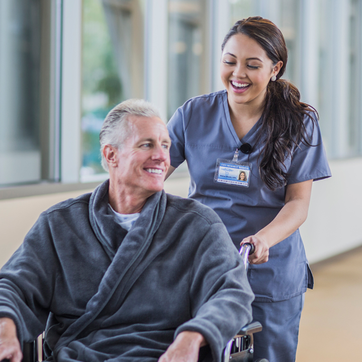 Female skilled nursing provider laughing as she pushes a male patient sitting on a wheelchair