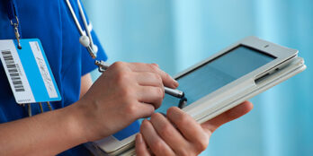 Close up of a medical professionals hands holding a tablet device and using a stylus to browse through content