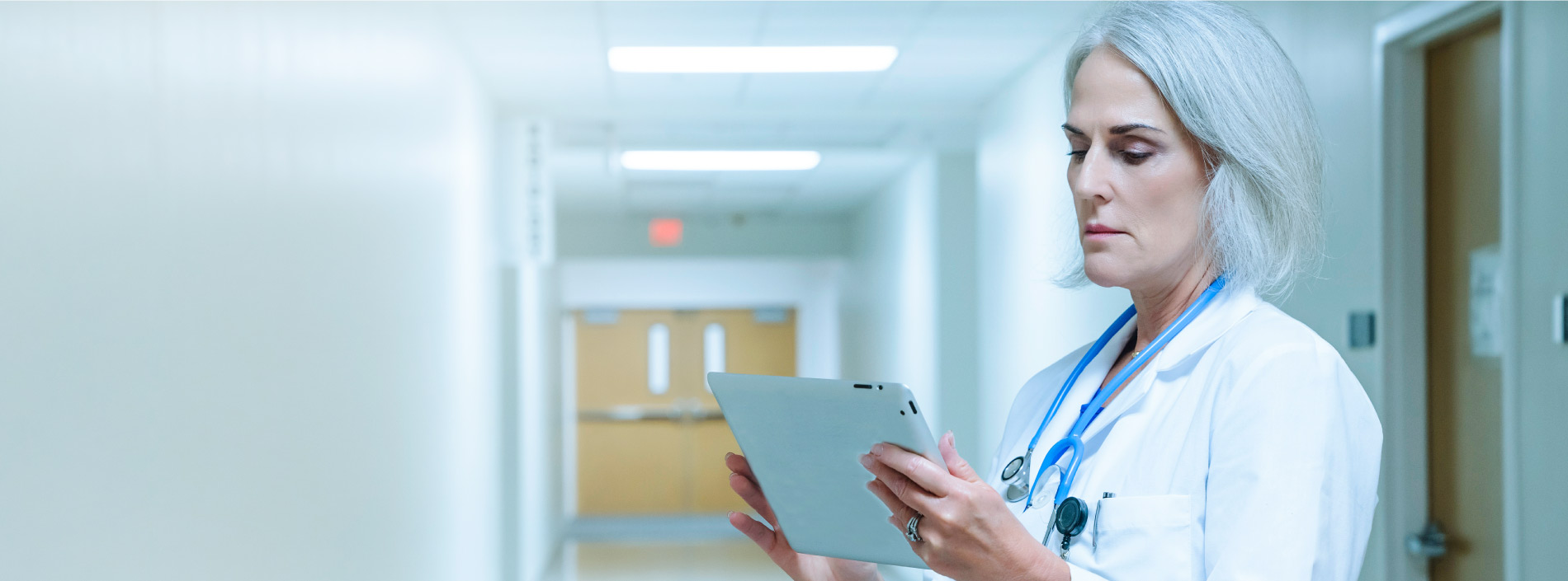 Female doctor standing in a hospital corridor and reviewing PAC Network Management data on a tablet device