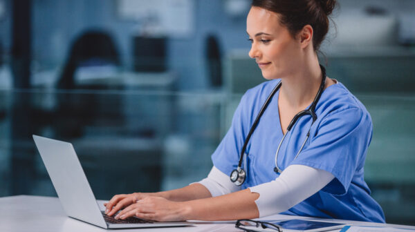 Female skilled nursing provider seated and using PointClickCare Connect software on a laptop