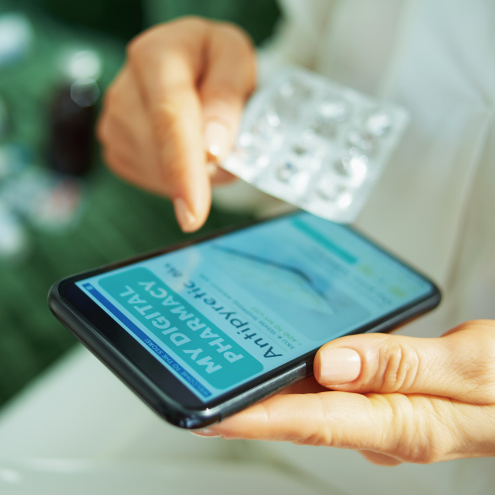 Close up of a mobile device displaying a digital pharmacy page and finished prescription medication being held